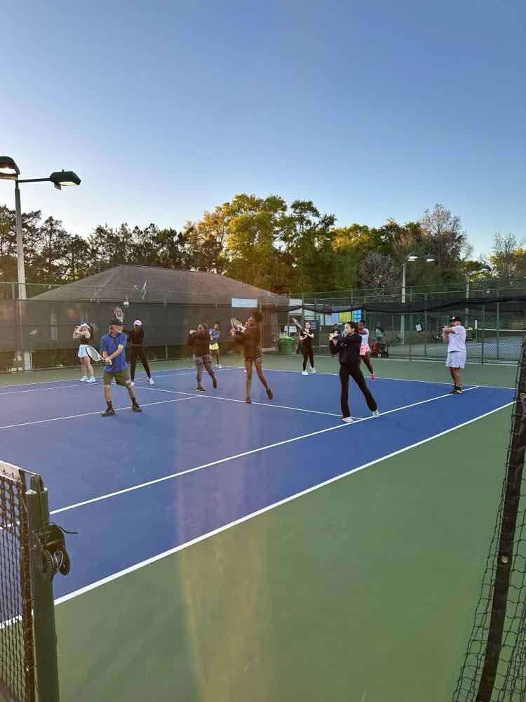 Players practicing strokes during a clinic on a blue court at sunset